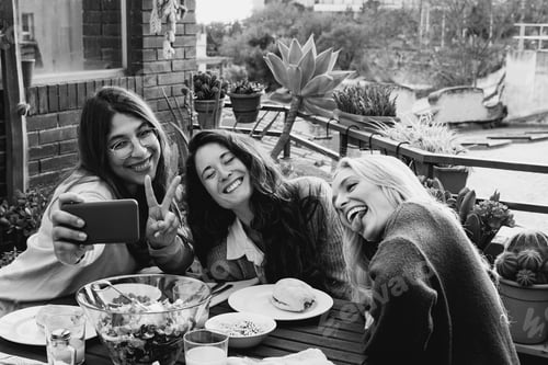 Preview: Happy multiracial friends using mobile phone at backyard vegan dinner party - Black and white edit