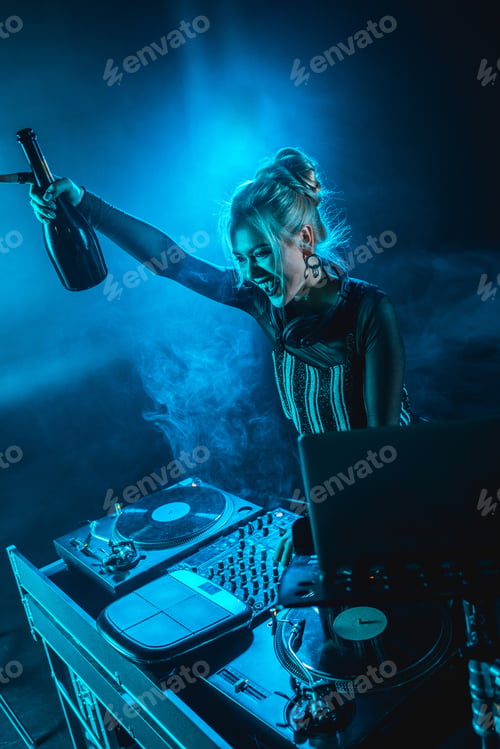 Preview: cheerful blonde dj woman holding bottle and smiling near dj equipment in nightclub with smoke