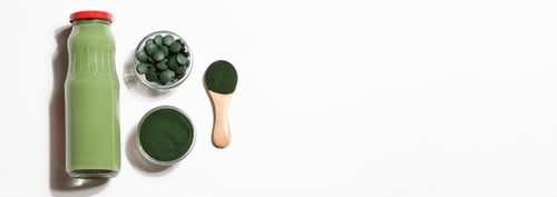 Preview: green smoothie in bottle and spirulina algae powder and pills in glass bowl on white background.