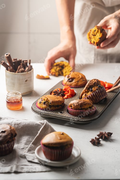 Preview: Homemade spicy pumpkin muffins or cupcakes with chocolate on a metal rack with woman hands