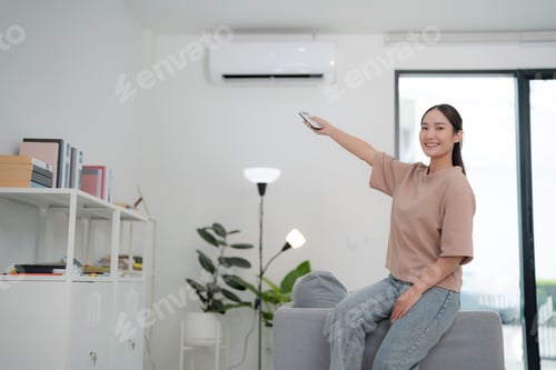 Preview: Young woman controlling air conditioner at home