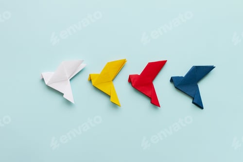 Preview: three paper origami pigeons white, ellow, red and blue in row on light background