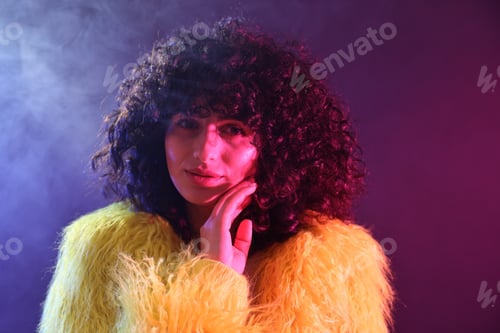 Preview: Beautiful young woman in yellow fur coat on color background in neon lights and smoke