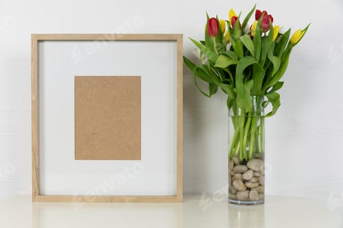 Preview: View of a picture frame, with red and yellow tulips placed in a glass vase on plain white background