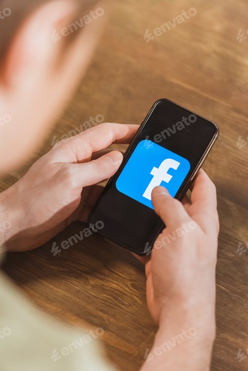 Preview: Man using smartphone with facebook logo icon on screen