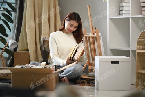 Preview: Happy young woman moving to new home and unpacking belongings. Relocating concept