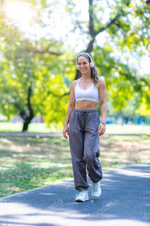 Preview: Woman walking outdoors in sports clothes, listening to music through headphones