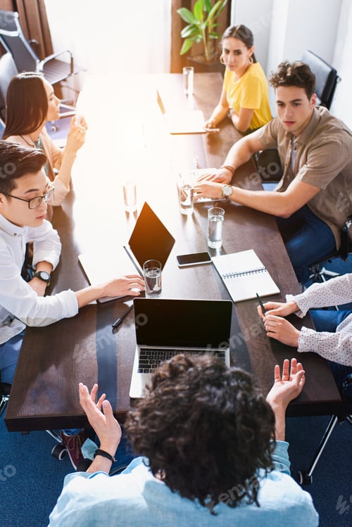 Preview: high angle view of multicultural business partners having meeting at table with laptops in modern