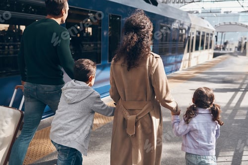 Preview: Rear view of family with two little kids walking by railroad station platform together