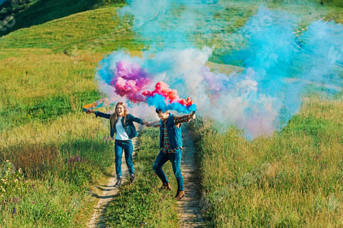 Preview: high angle view of couple holding colorful smoke bombs on rural meadow