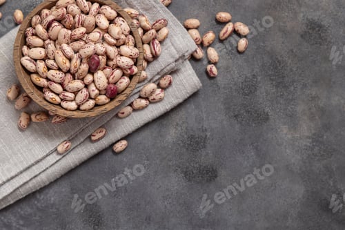 Preview: Wooden bowl full of dried pinto beans on napkin on gray top view. Traditional Latin American legumes