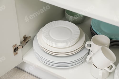 Preview: Clean plates and cups on shelf in cabinet indoors