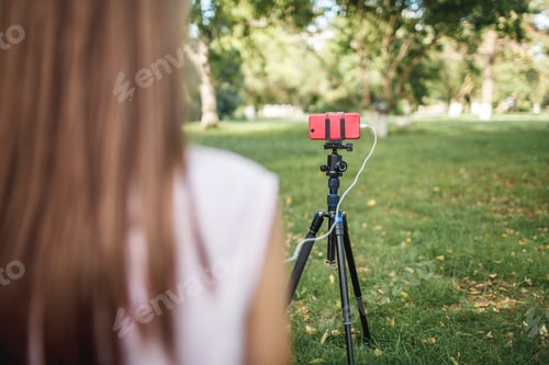 Preview: Woman working with camera phone on tripod on a meadow