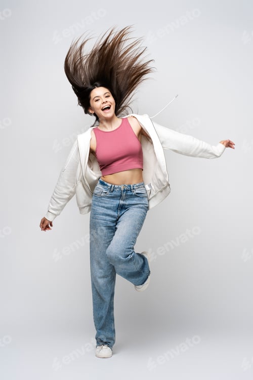 Preview: Portrait of attractive latin teenage girl in casual clothes jumping, isolated on gray background