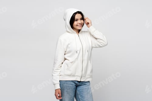 Preview: Smiling teenage girl wearing hood on head, standing isolated on gray background, looking away