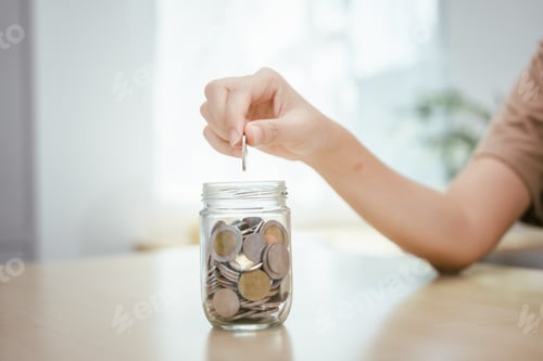 Preview: A young woman saves money for the future by putting coins in a piggy bank on the table, managing
