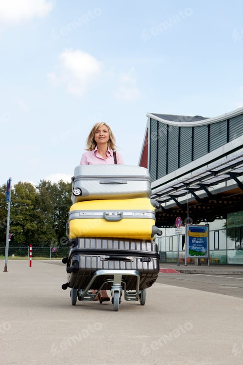 Preview: Mid adult woman pushing luggage trolley to airport