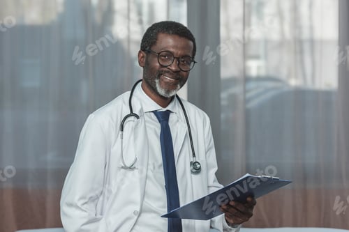 Preview: Smiling african american doctor standing with clipboard and looking at camera