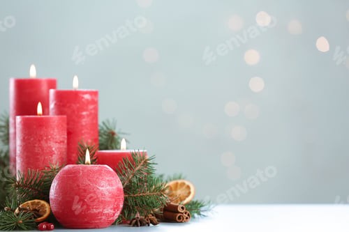 Preview: Burning red candles with Christmas decor on table against blurred lights. Space for text
