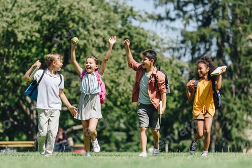 Preview: four excited schoolkids gesturing with raised hands while running on lawn in park