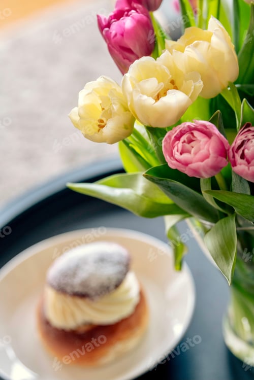 Preview: Flowers in a selective focus with Semla sweet roll blurred in the background, laskiaispulla