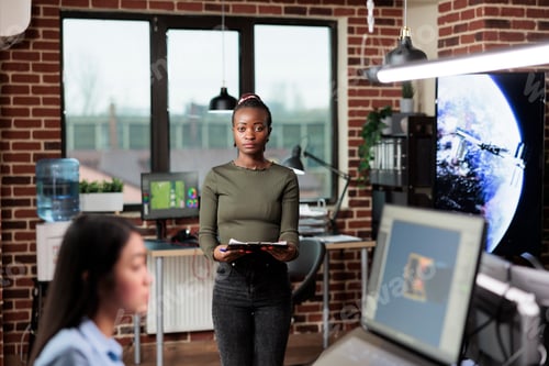 Preview: Creative agency office worker standing in workspace, looking at camera while having clipboard.