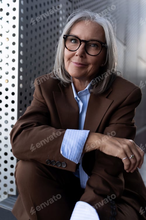 Preview: 60 years old successful slender gray-haired business woman dressed in a stylish brown jacket is