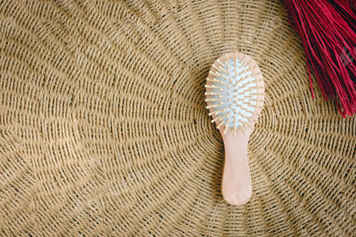 Preview: Small round wooden natural hair comb against the background of a wicker basket. Hair care.