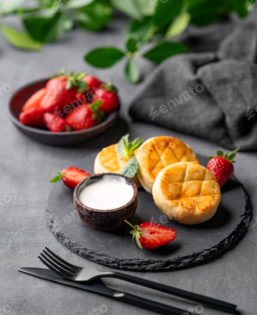 Preview: Cottage cheese, cheesecakes or syrniki with sour cream, strawberries, leaves on a black slate
