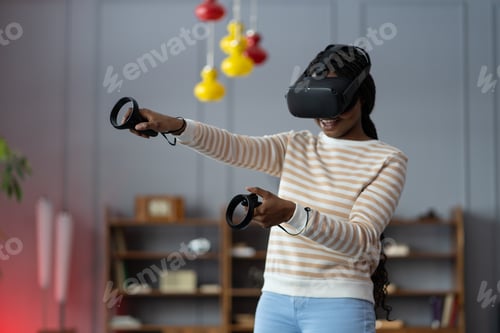 Preview: Happy young african american woman wearing virtual reality goggles playing video games at home