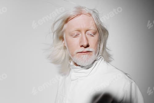 Preview: Man with white hair and beard, wearing a white outfit, against a plain light gray background