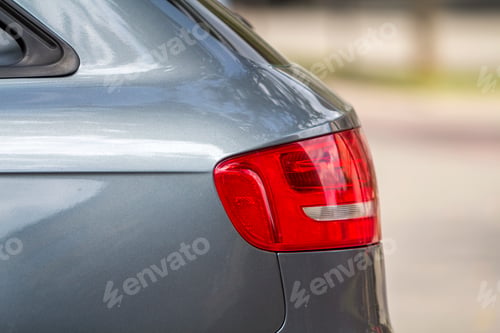 Preview: Side view detail of red stop lights of shiny luxurious silver car on blurred copy space background