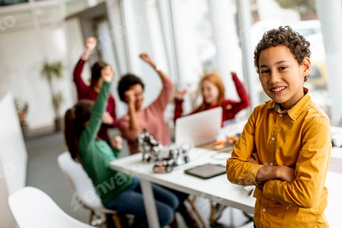 Preview: Cute little boy standing in front of kids programming electric toys and robots at robotics classroom