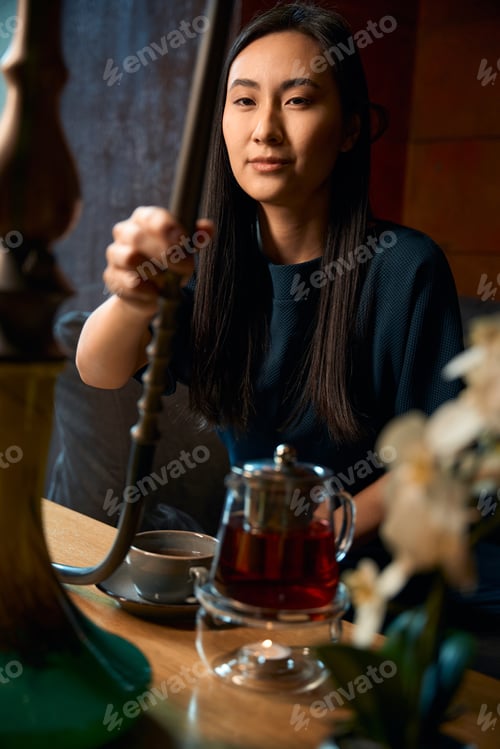 Preview: Excited Asian woman holding smoking pipe, enjoying scented hookah