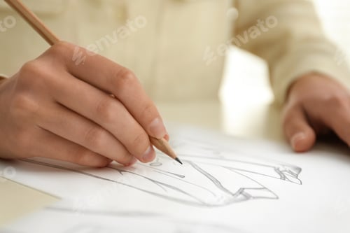 Preview: Woman drawing clothes with pencil on sheet of paper at white table, closeup
