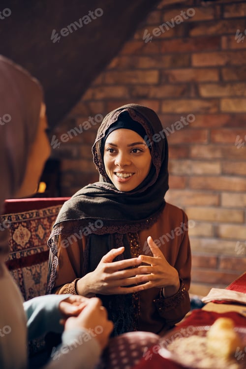 Preview: Happy Middle Eastern woman in traditional clothing talking to female friend at home.