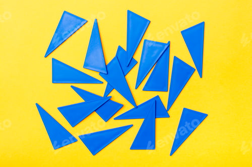 Preview: Blue plastic flat triangles are scattered chaotically on a yellow background. Top View