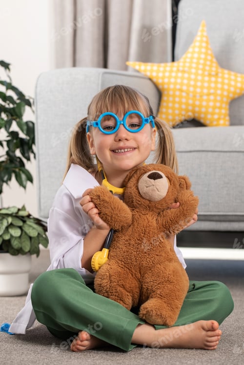 Preview: A little girl is playing in a doctor costume with a teddy bear. A child is playing at the hospital.