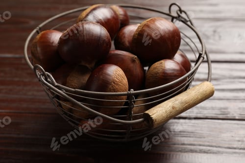 Preview: Sweet fresh edible chestnuts in metal basket on wooden table, closeup