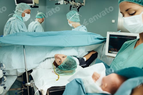 Preview: Operating room nurse bringing baby to mother while team finishing c-section