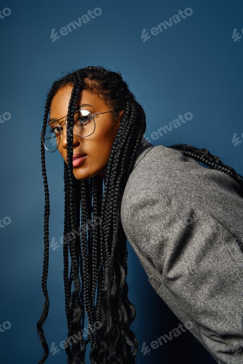 Preview: Young woman with long braids leans slightly, flaunting her stylish glasses and confidence.