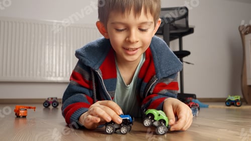 Preview: Portrait of cute boy lying on floor and playing with two toy cars. Children playing games at home.