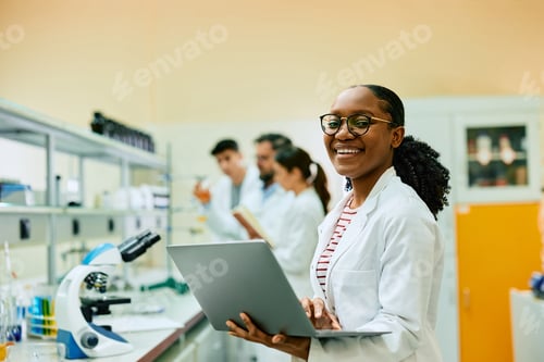 Preview: Happy black biochemist working on laptop in a lab and looking at camera.