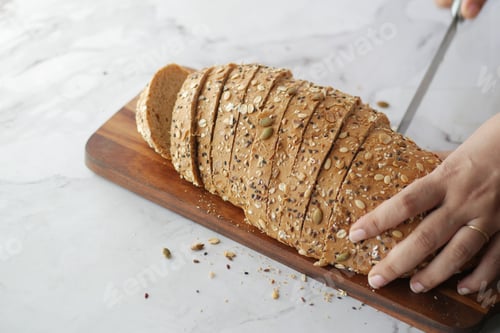 Preview: Women hand cutting baked brow bread on table.