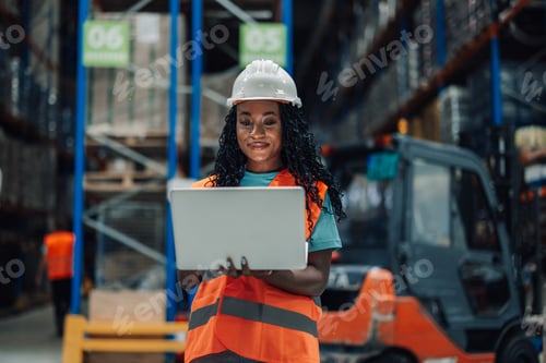 Preview: Female warehouse worker using laptop standing in busy warehouse