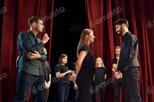 Preview: Two people talking. Group of actors in dark colored clothes on rehearsal in the theater