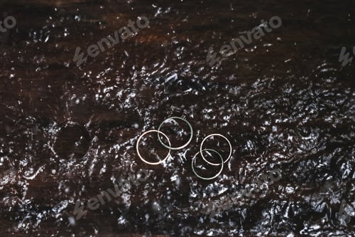 Preview: Double white gold wedding rings under water drops splash close up. Studio macro shot