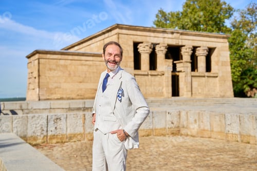 Preview: Smiling man in a striped suit posing near an ancient stone temple outdoors