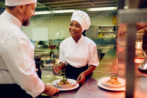 Preview: Happy black cook and her coworker decorating a plate while serving food in a restaurant.