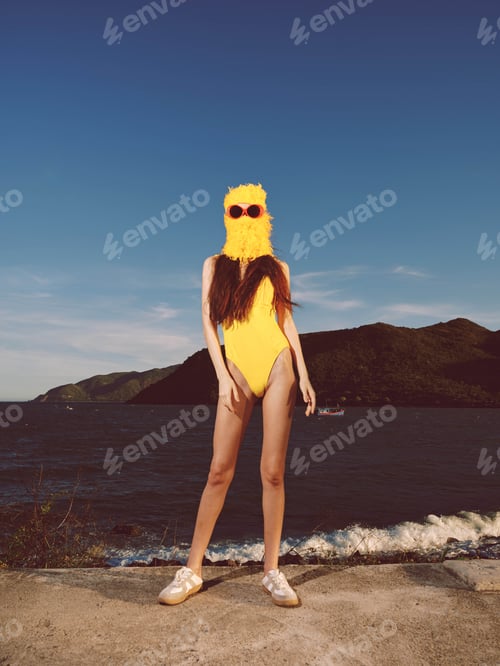 Preview: Woman in yellow swimsuit and sunglasses standing on a rock near a serene body of water with a